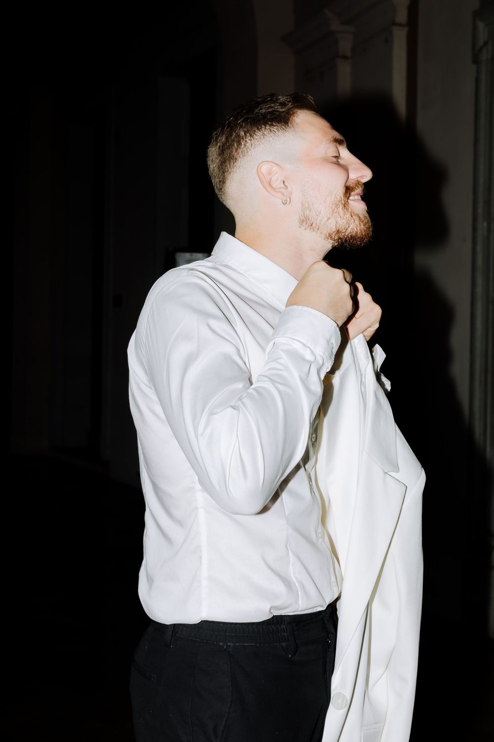 A person in a white dress shirt adjusting their collar against a dark background.