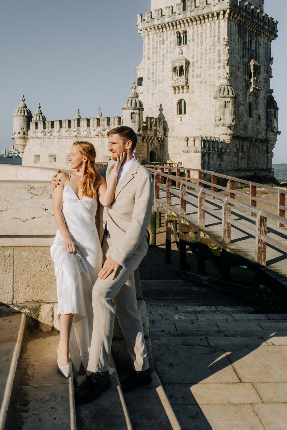 Couple elegantly posed in white attire at Belem Tower in Lisbon Portugal during romantic photoshoot.