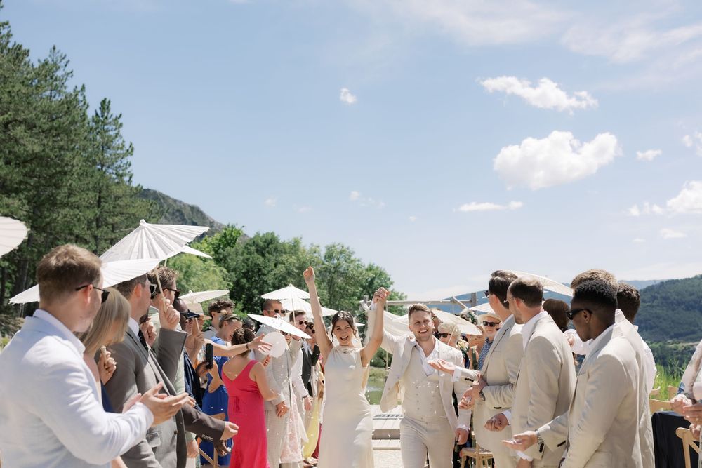 Wedding guests celebrating newlyweds with raised hands at outdoor ceremony in scenic countryside venue.