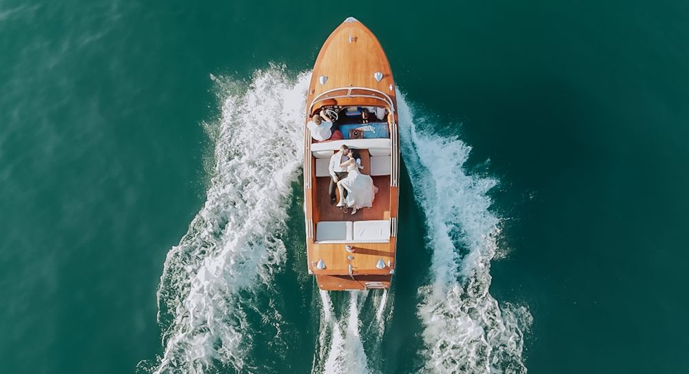 Aerial view of a wooden boat cruising through turquoise waters creating white wake patterns.