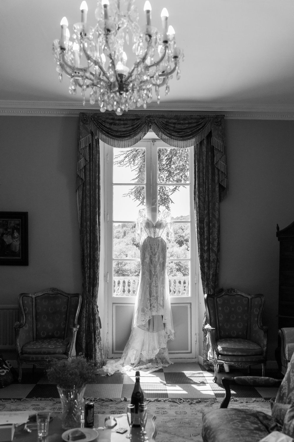 Elegant chandelier in a luxurious room with tall windows and ornate drapes creates a romantic atmosphere in black and white.