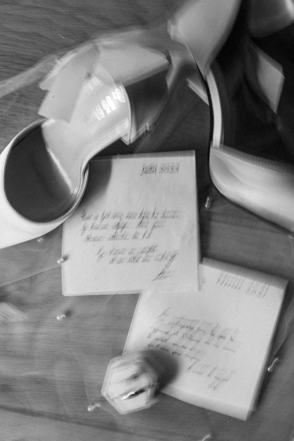 A black and white still life of high heel shoes and handwritten notes on a wooden surface.