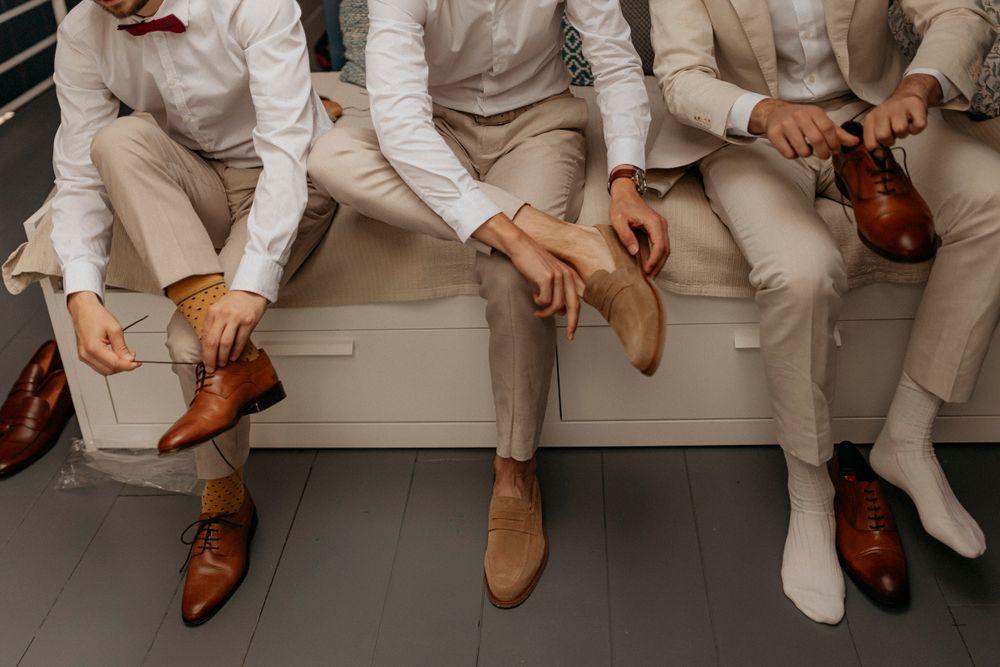 A detail shot of men's dress shoes and legs in light-colored suits sitting on a bench.