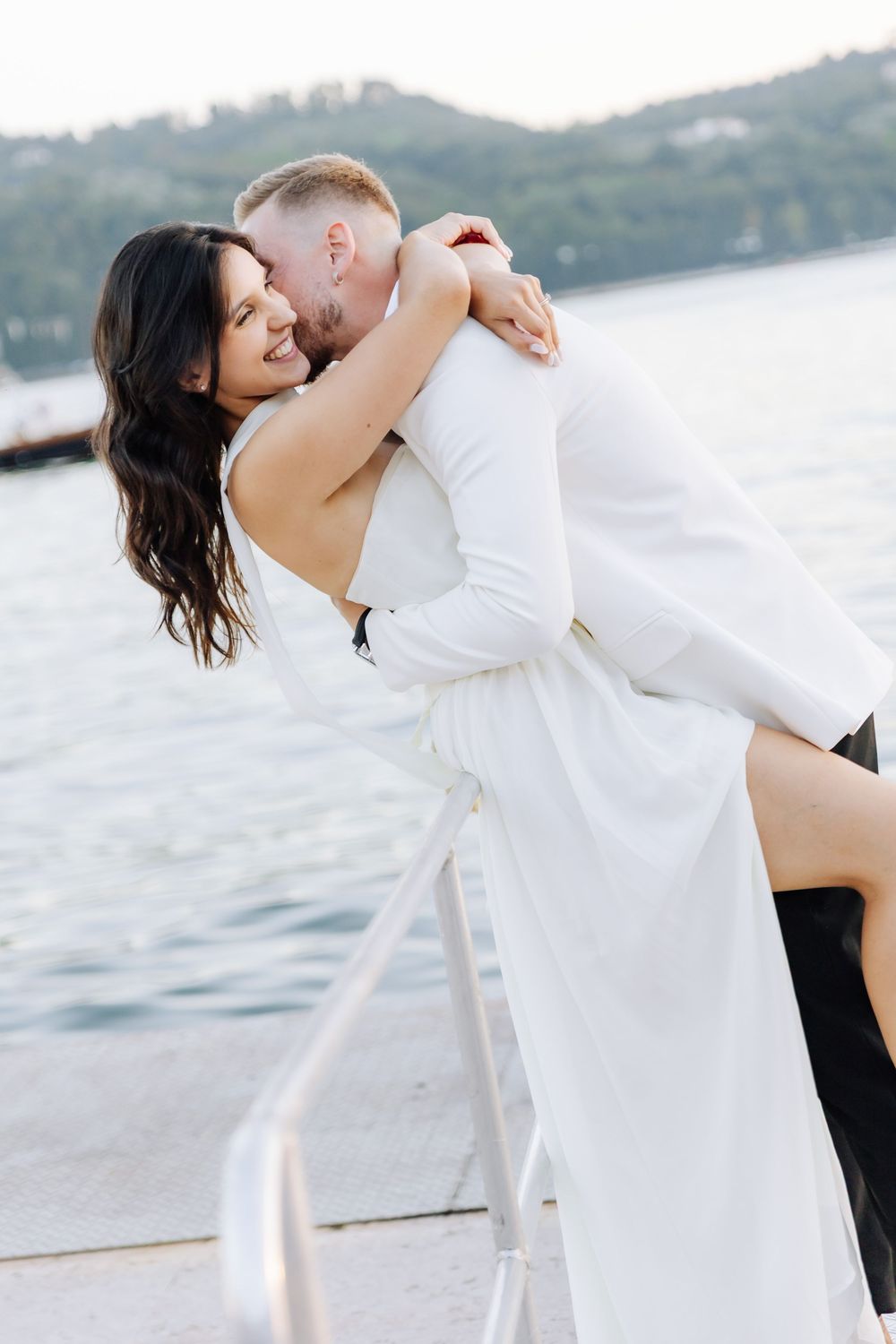 A romantic moment between newlyweds embracing on a boat deck with mountains in the background.