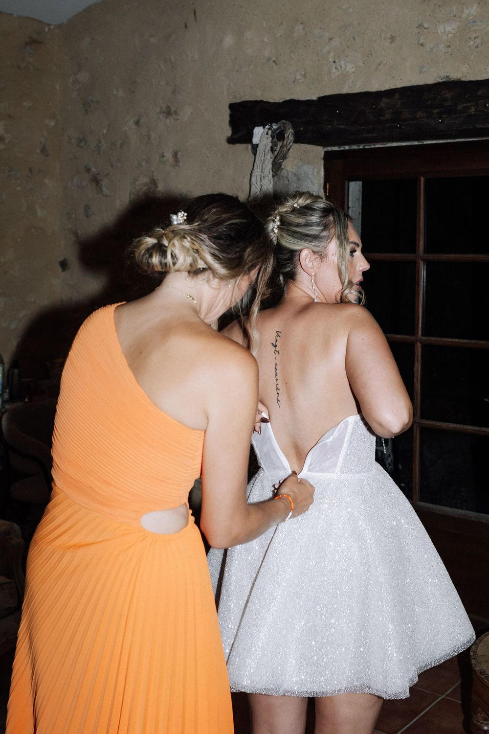 Two people in formal attire, one wearing an orange dress and one in white, at what appears to be a party or event.
