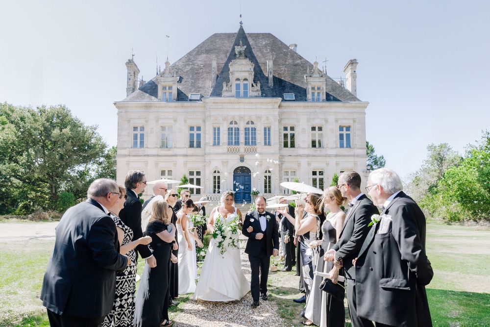 Elegant outdoor wedding ceremony and reception at a grand French chateau with guests celebrating in formal attire.