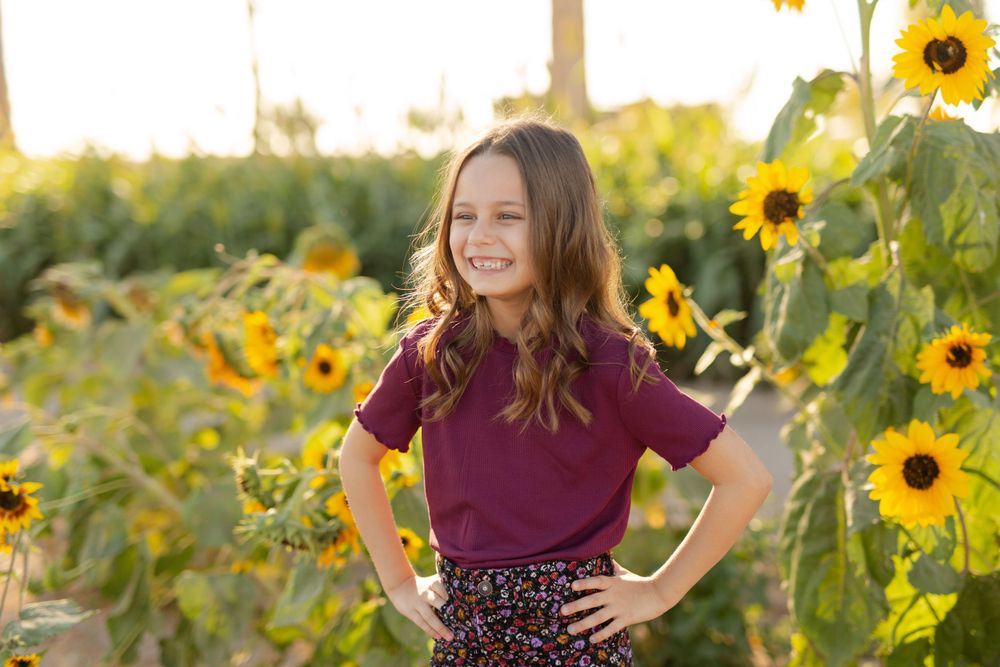 Portrait of youth in burgundy top and patterned skirt posing confidently among tall sunflowers.