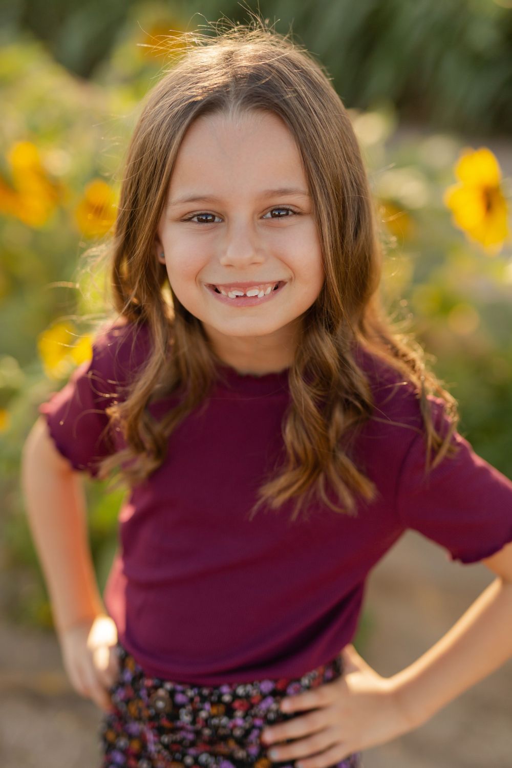 Close-up portrait in a sunflower field with burgundy shirt and floral pattern skirt.