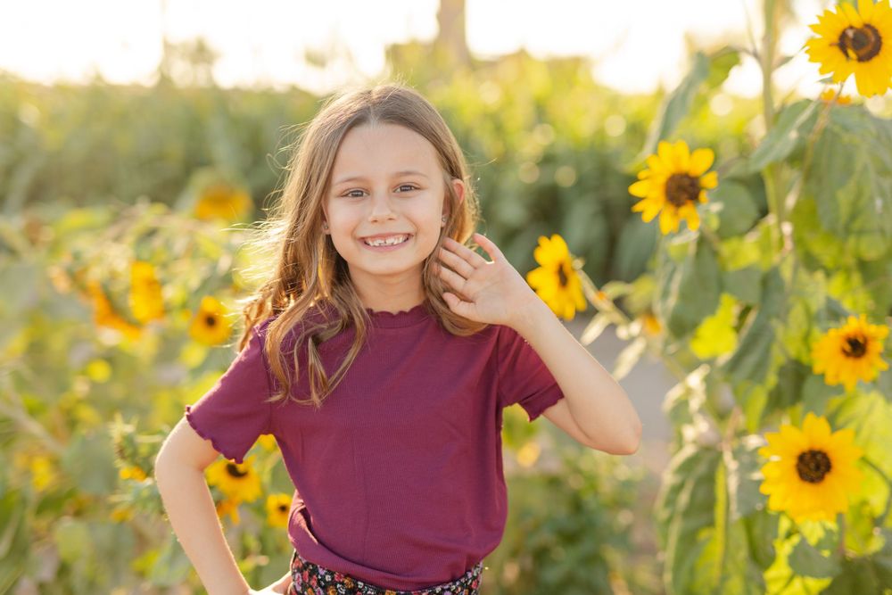 Natural outdoor portrait against sunflowers with burgundy shirt and flowing hair.