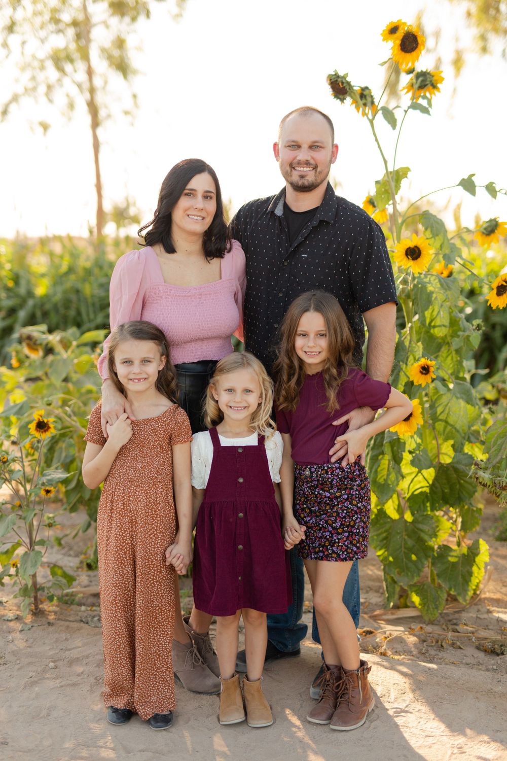 A family poses together with bright sunflowers blooming behind them.