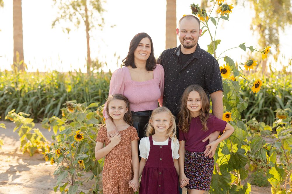 A family portrait taken in front of tall sunflowers on a bright sunny day.