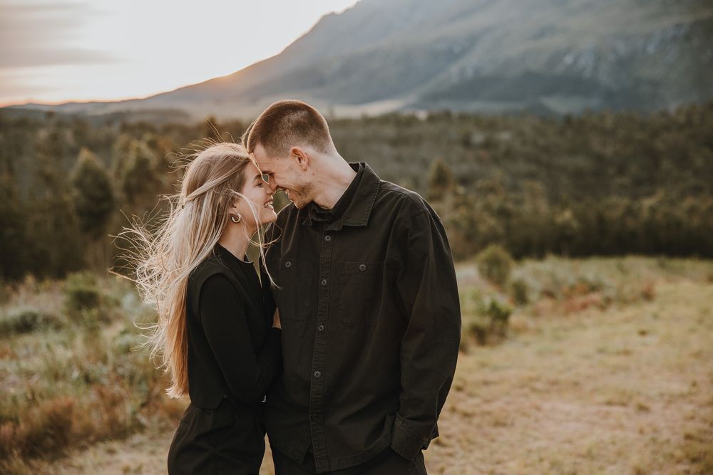 Romantic couple in black outfits sharing an intimate moment outdoors with mountain scenery and golden sunset light.