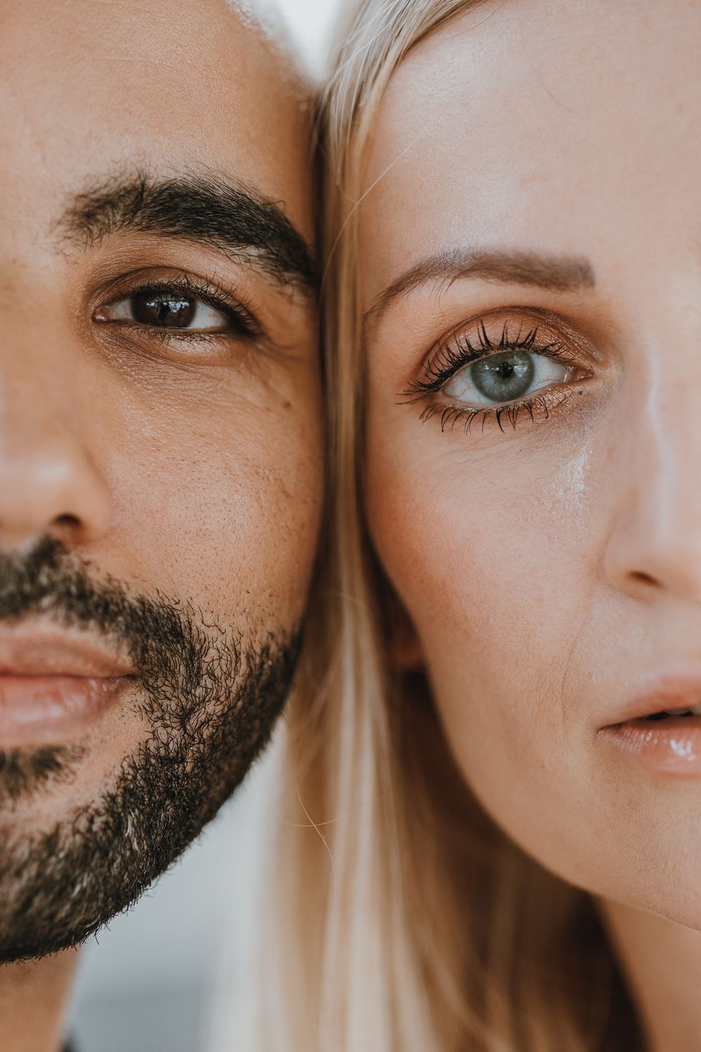 Close-up portrait of a bearded man and blonde woman with blue eyes facing each other cheek to cheek.
