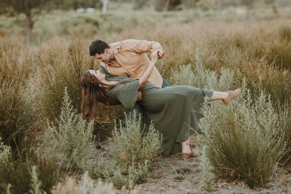 Romantic couple sharing a kiss in a lush green field, man dipping woman in a tender embrace outdoors.