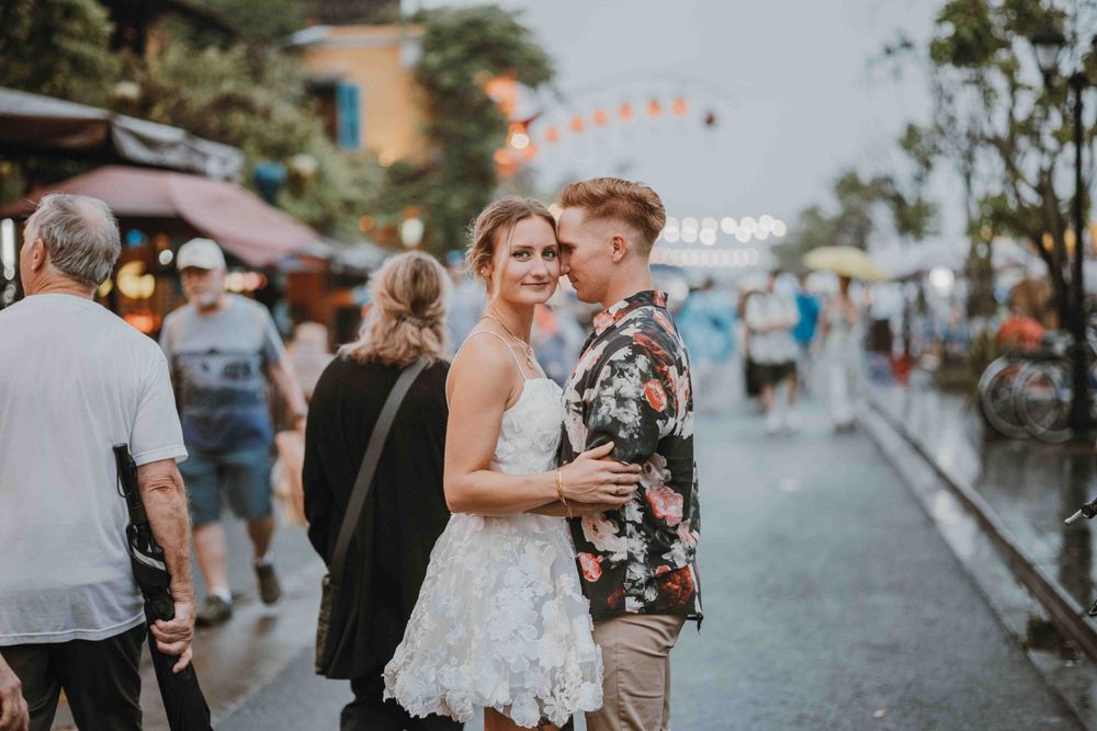 A couple shares an intimate moment at a lively street festival with string lights and vendors in the background.