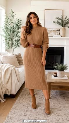 Woman wearing camel ribbed turtleneck midi sweater dress with brown leather belt and matching ankle boots indoors.