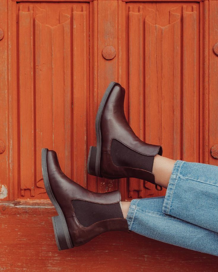 Black ankle boots styled with blue jeans against a rustic red wooden background.