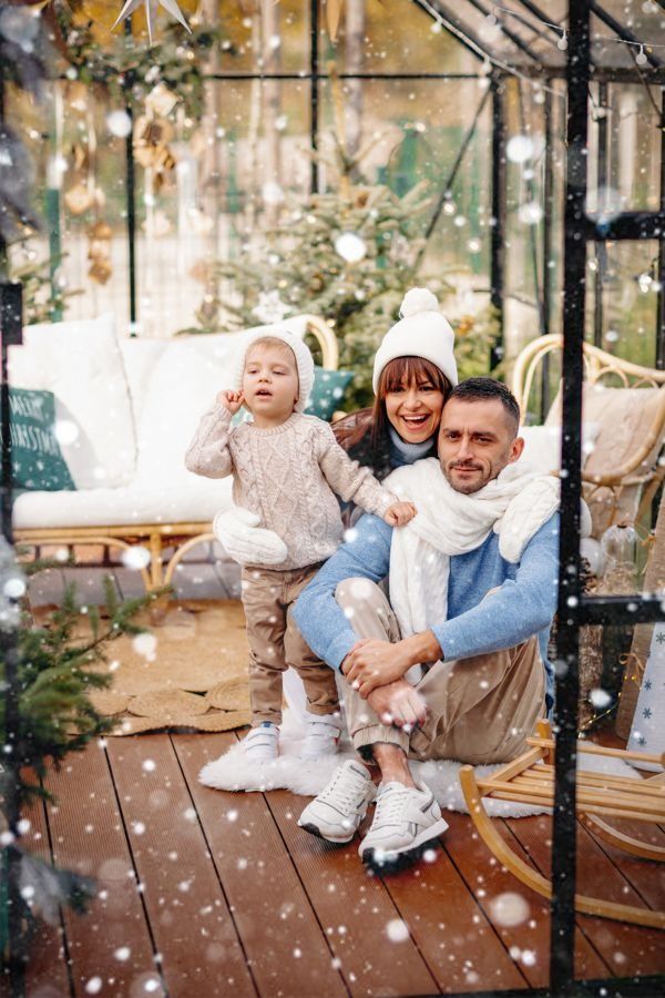 A happy family captures playful moments in a greenhouse setting with falling snow.