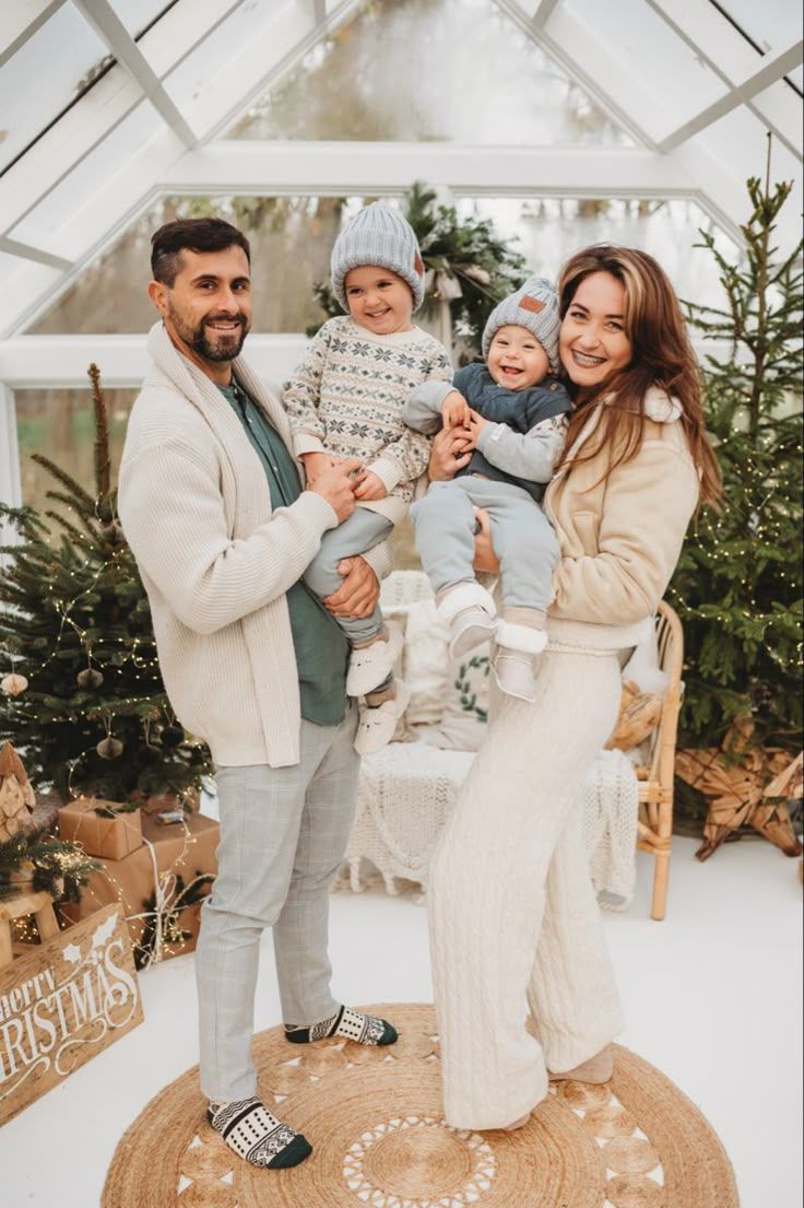 Family holiday portraits in cozy neutral outfits against a winter greenhouse backdrop.