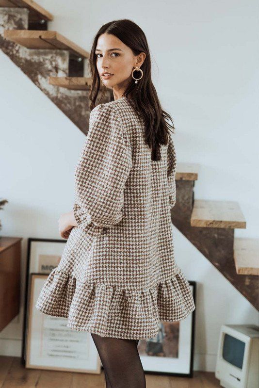 Fashion model showcasing a romantic beige gingham top with ruffle details and balloon sleeves against a white wall.
