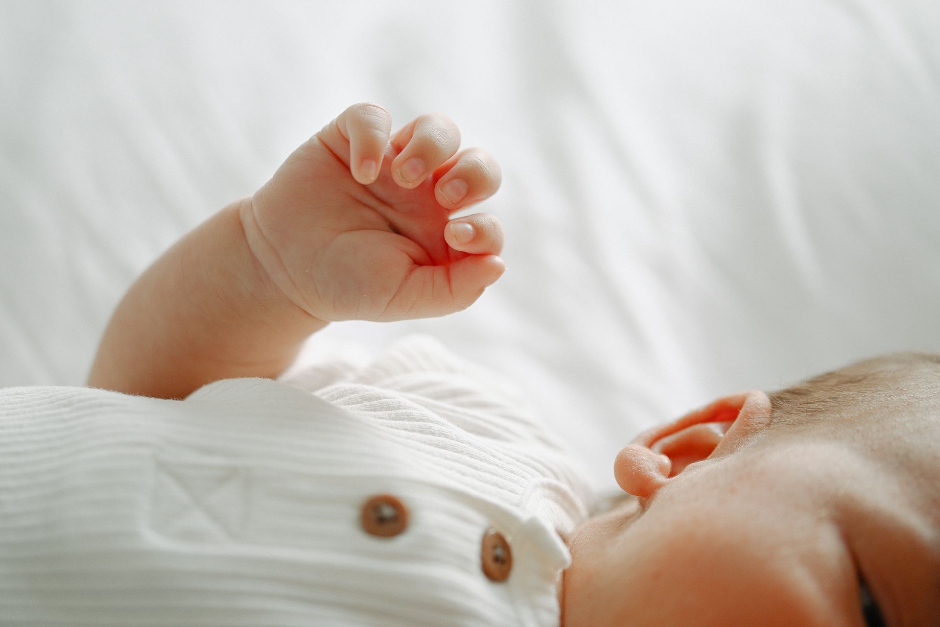 A close-up view of a baby's tiny hand reaching up against a white background.