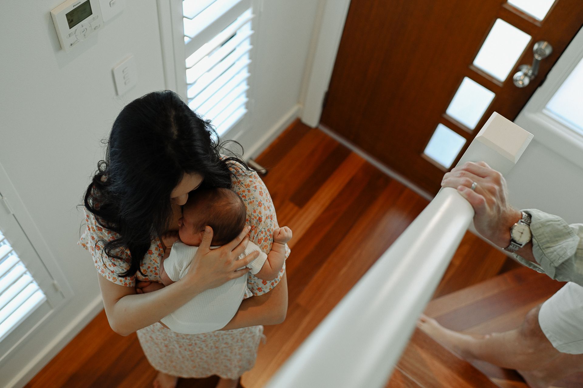 Bride in a white lace dress adjusts her hair while standing on hardwood floors near a window.