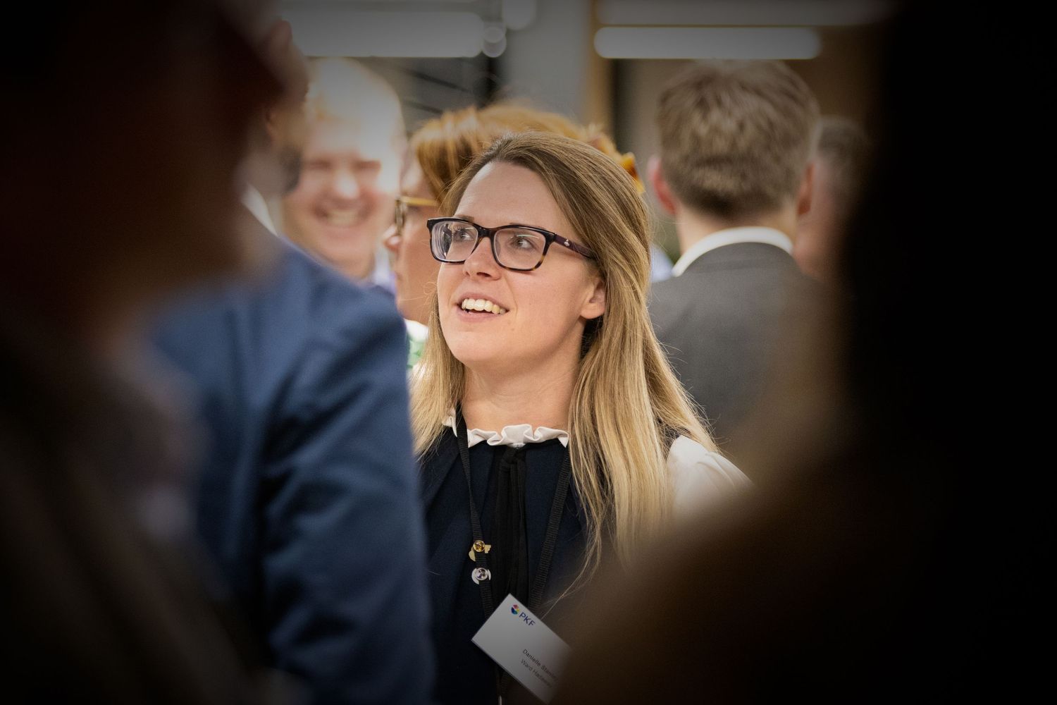Smiling young woman with glasses and long blonde hair at a professional networking event.