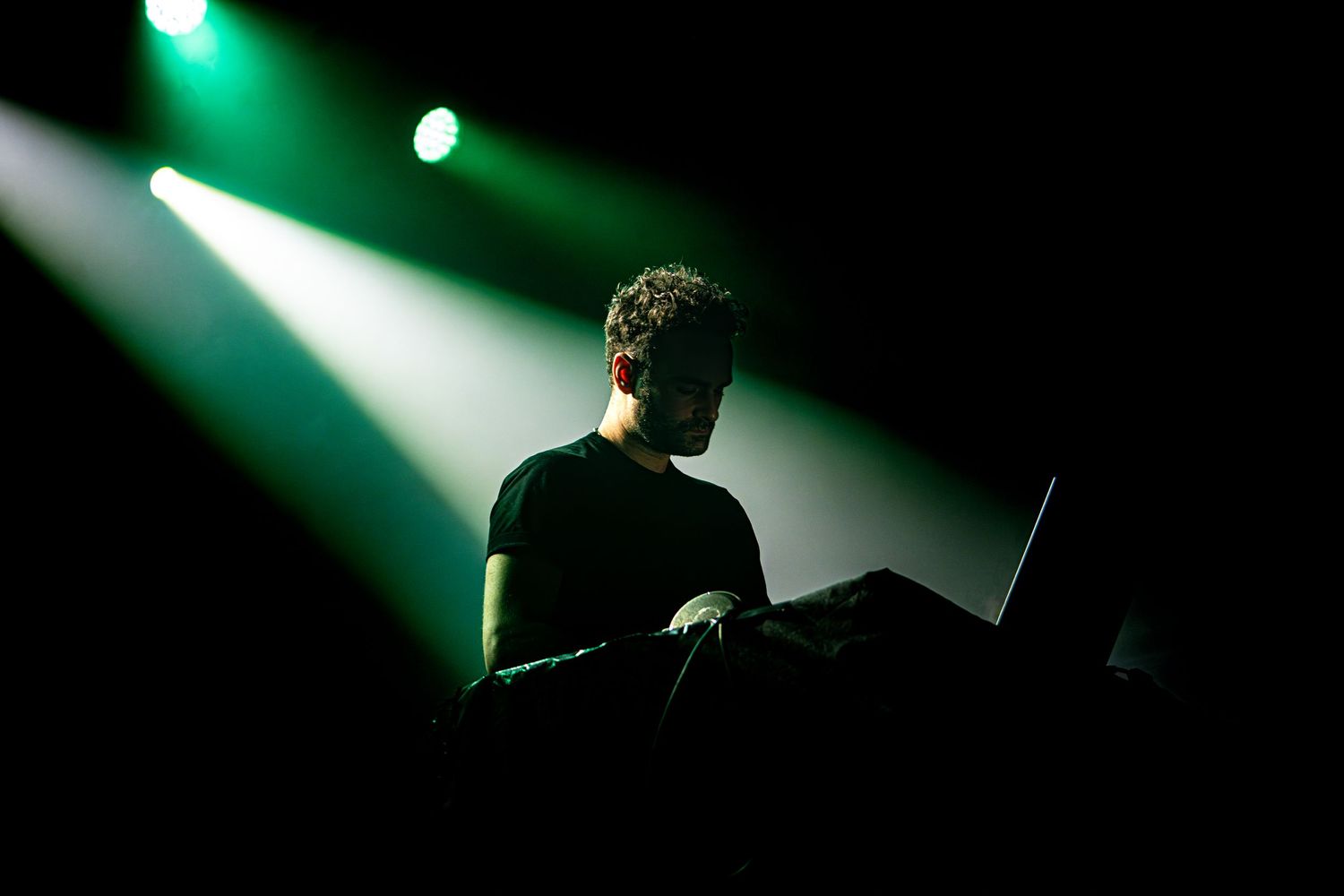 Silhouetted DJ performing on stage with green spotlights in dark atmosphere.