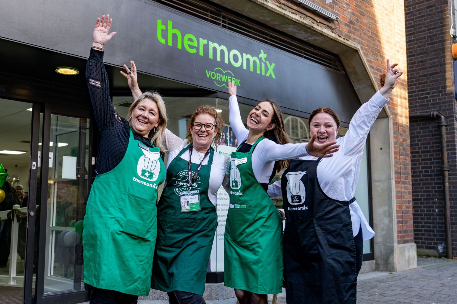 Thermomix store employees in green aprons celebrating with raised arms.