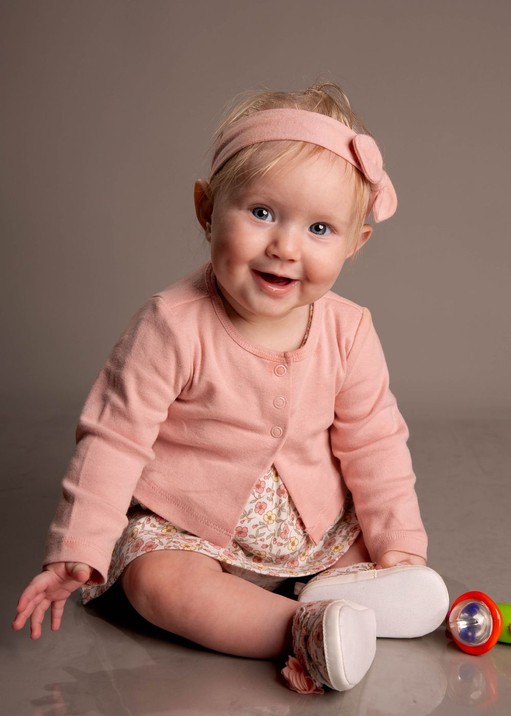 Baby in pink sweater sitting on light gray backdrop with small toy balls at various sitting poses and angles.