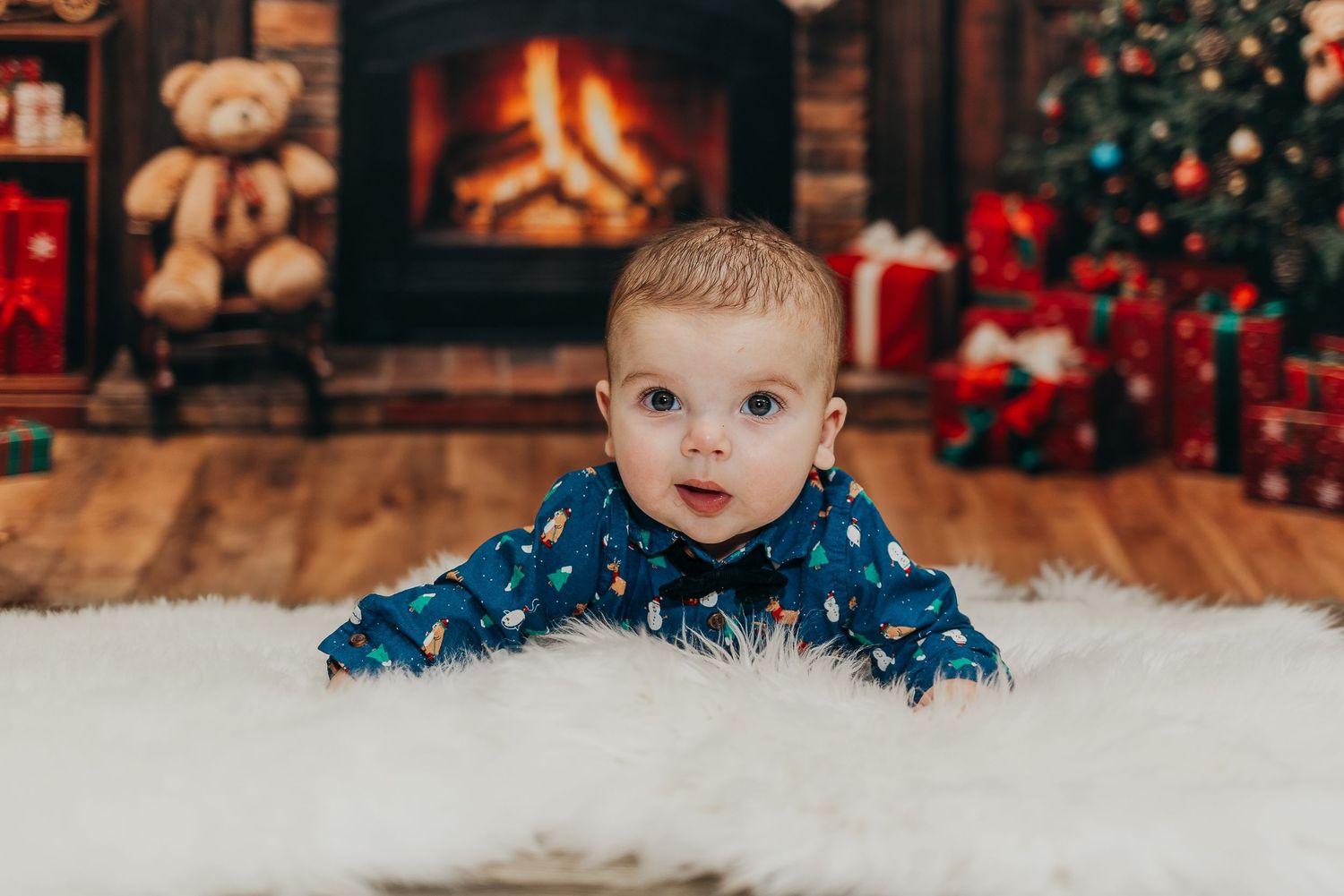 A joyful baby lies in autumn leaves with a brown headband and blue overalls during a fall photoshoot.