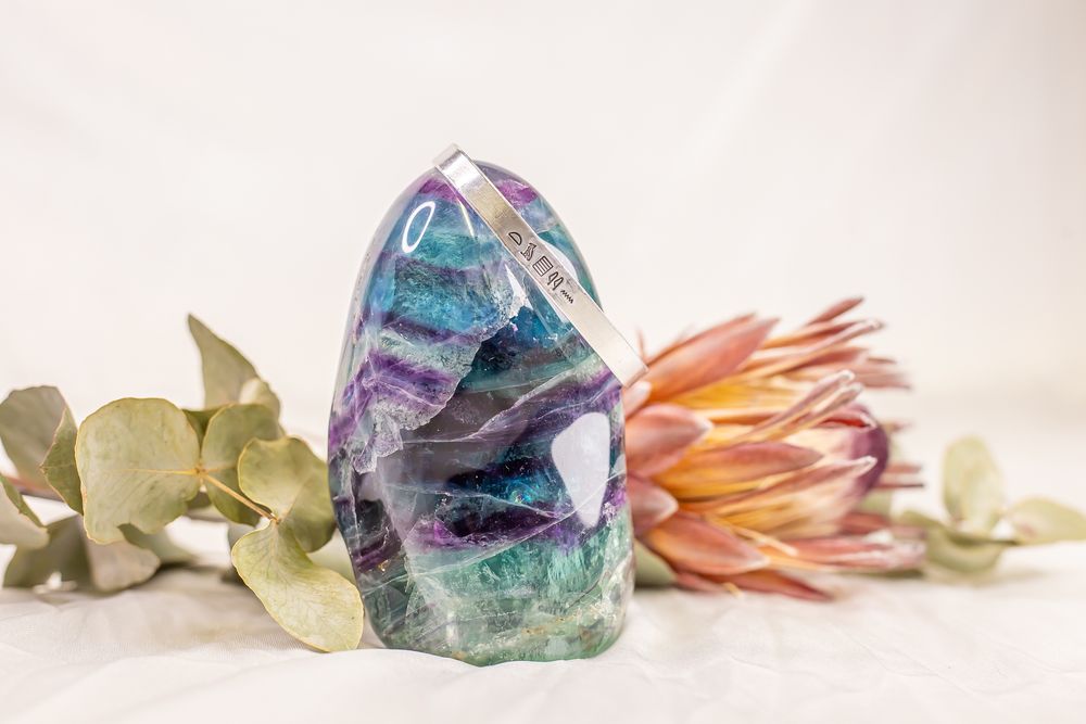 A collection of colorful crystals and dried flowers arranged in a soft, ethereal composition against a white background.