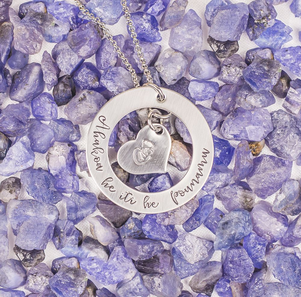 Silver circle pendant with heart charm displayed on scattered purple tanzanite crystal stones.