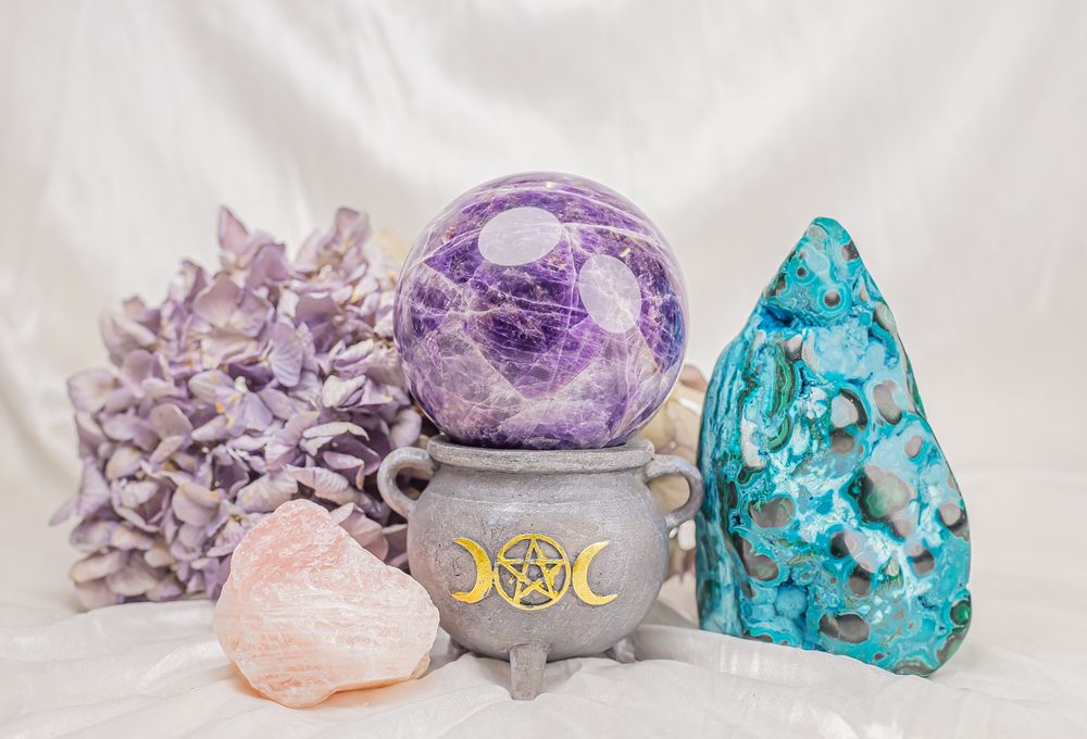 Colorful collection of raw crystals and minerals in purple, turquoise and pink hues arranged on white background.