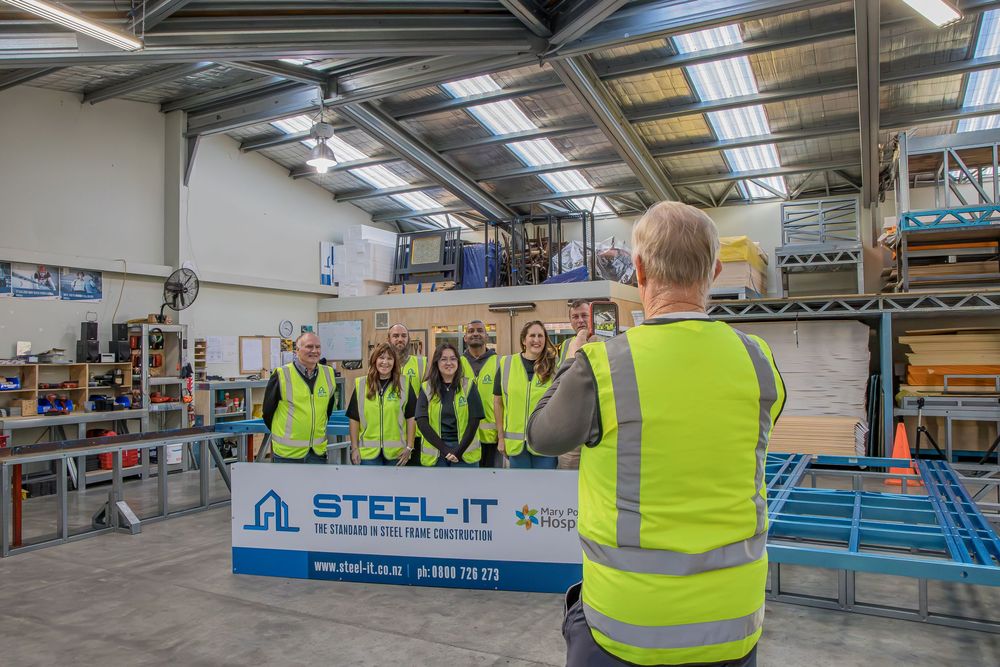 Group tour inside Steel-It manufacturing facility, with staff in hi-vis vests listening to a presenter near branded signage.