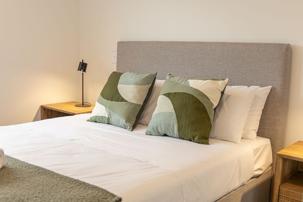 Modern bedroom with gray upholstered headboard, white bedding, and green geometric decorative pillows on a neatly made bed.