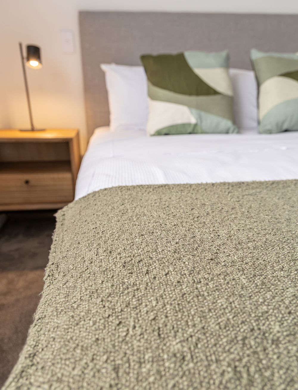 Close-up of a sage green textured throw blanket on a neatly made bed with white and green pillows.