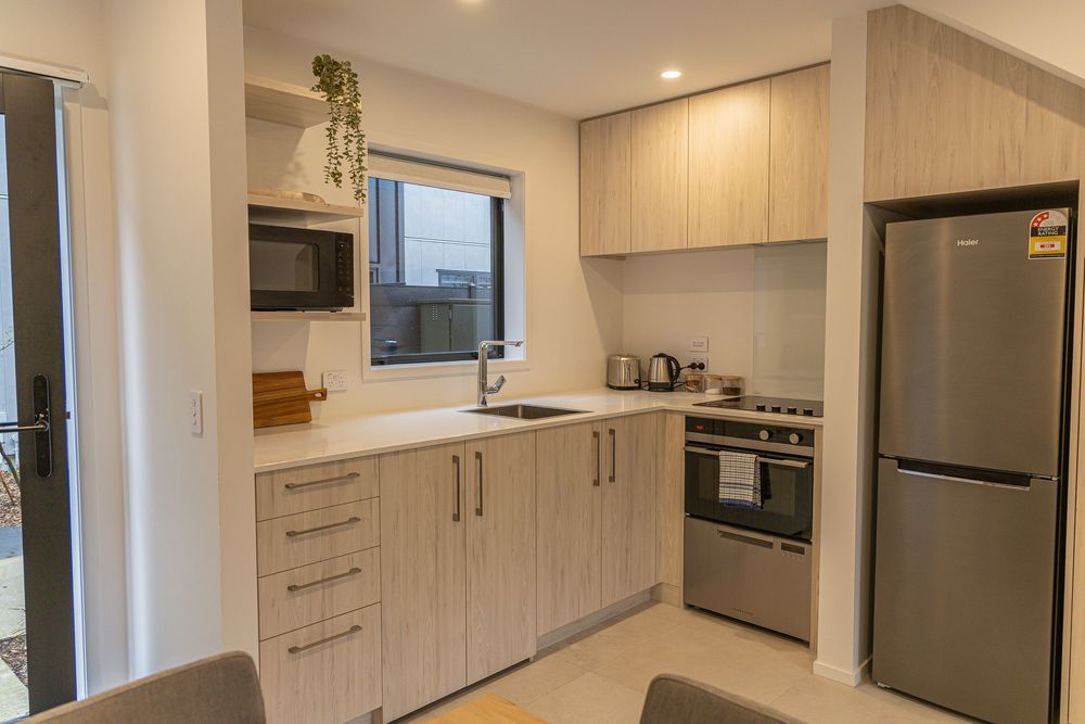 Modern compact kitchen with light wood cabinets, stainless steel appliances, built-in oven, and fridge in a bright apartment.