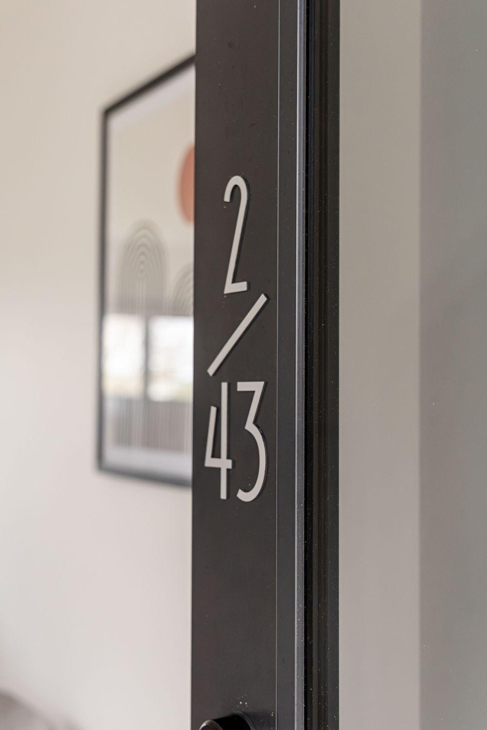 Close-up of a dark door frame with white number 2/43 signage, with framed artwork visible in the background.