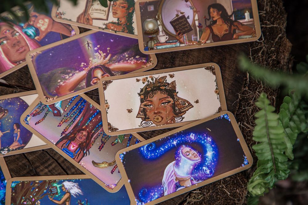 A collection of colorful illustrated oracle or tarot cards scattered on a dark surface with mystical artwork designs.