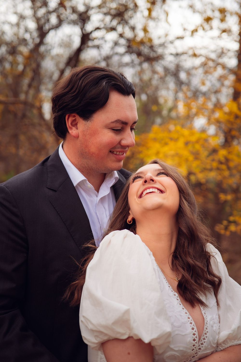 Joyful laughter shared between couple during outdoor autumn photoshoot.