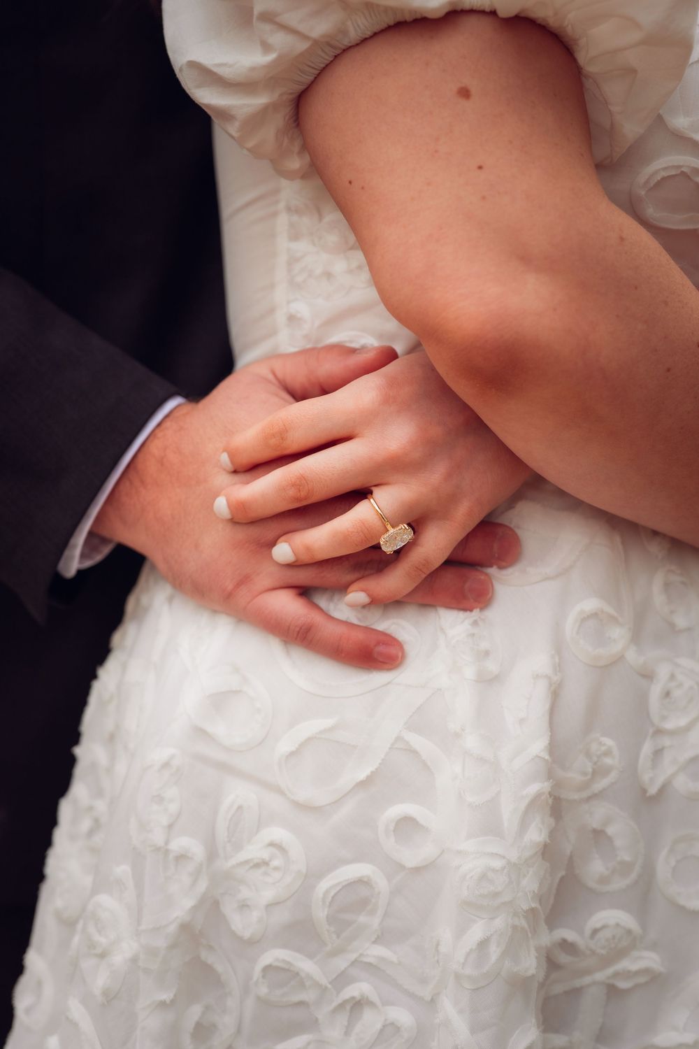 Detail shot of hands against white lace wedding dress fabric.