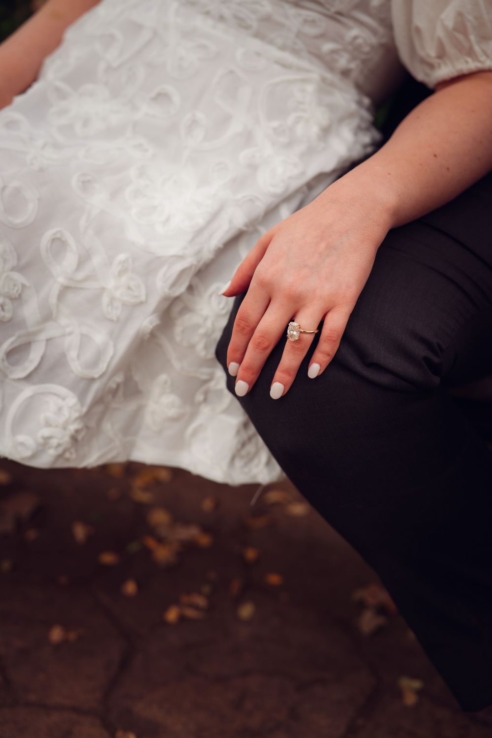Wedding ring detail shot with white lace dress in background.