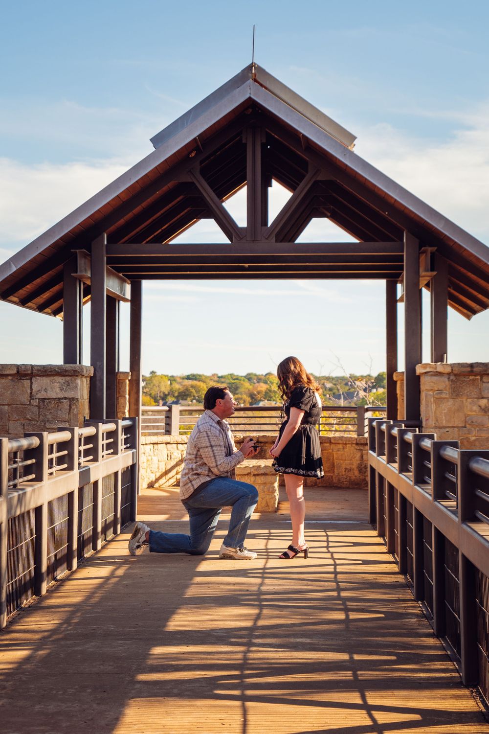 A proposal moment captured on a wooden bridge overlook during golden hour.