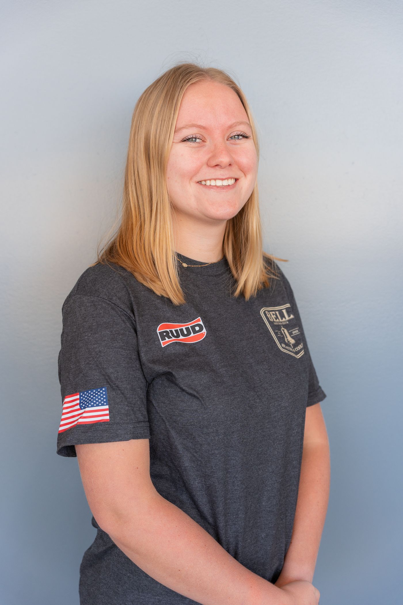 Person wearing dark grey t-shirt with American flag patch posing against grey background.