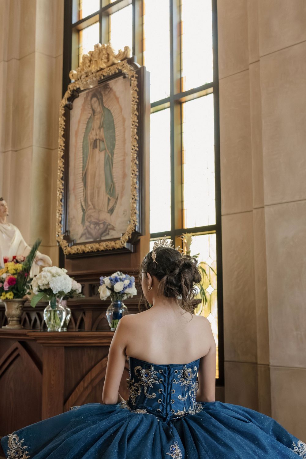 Elegant teal quinceañera gown photographed in a church interior with stained glass windows and religious artwork.