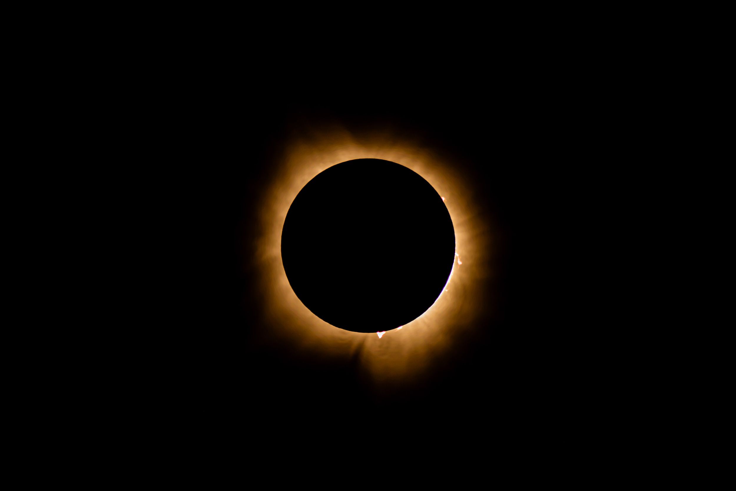 Total solar eclipse showing corona glowing around dark moon silhouette against black sky.