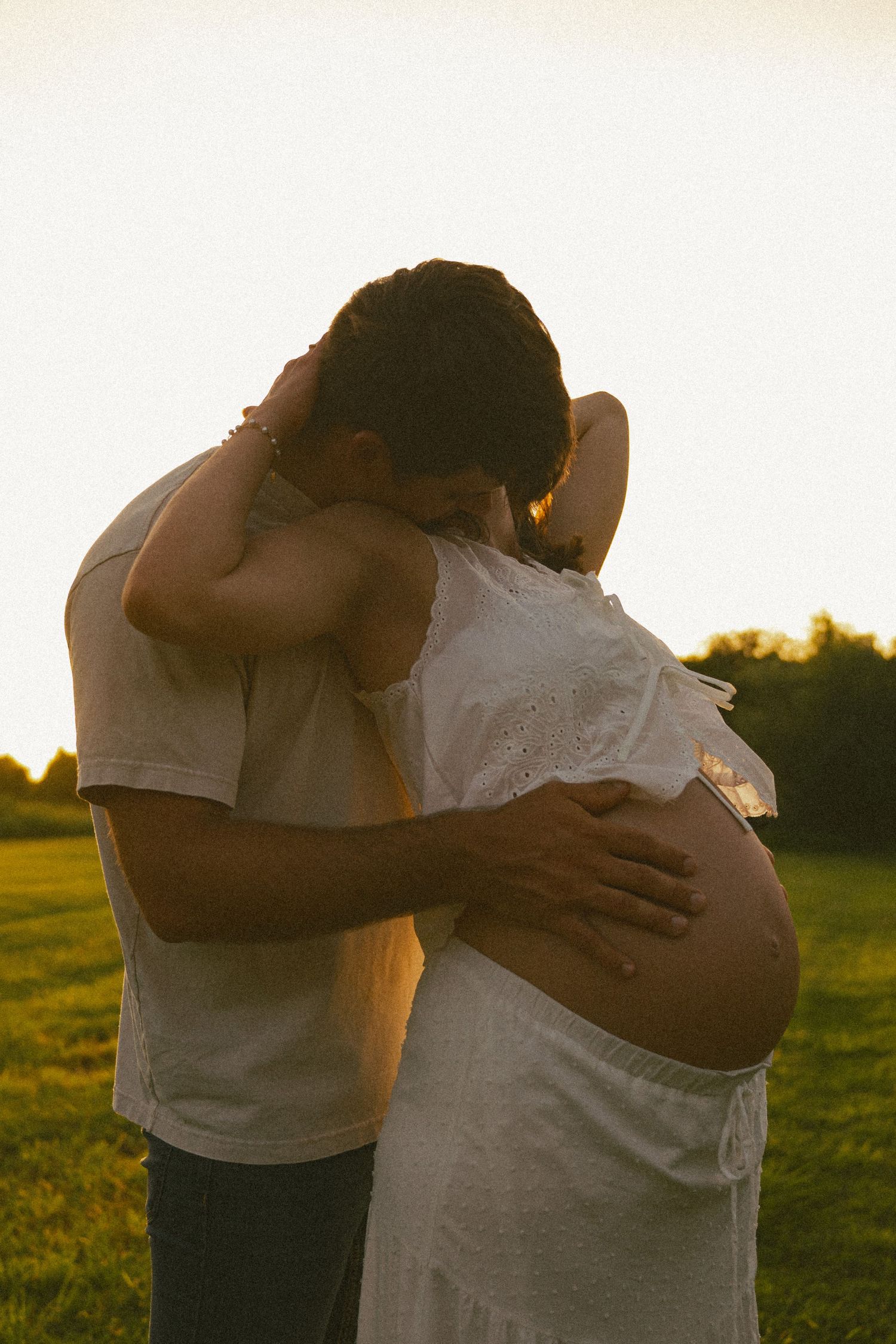 A tender embrace between a couple backlit by golden sunset light in a field.
