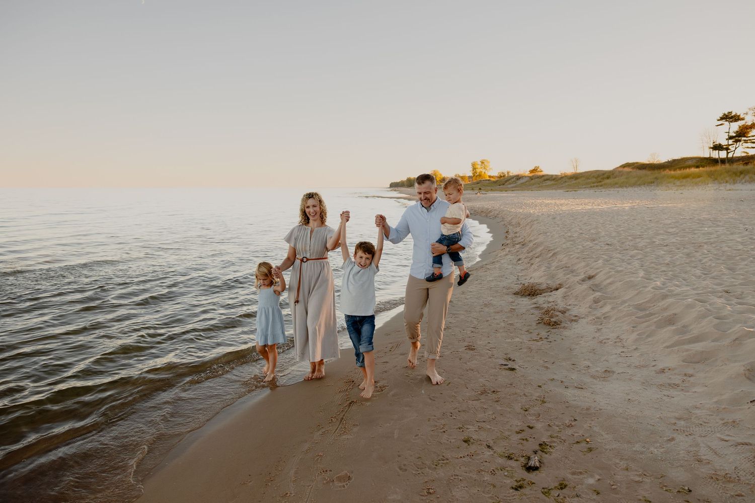 A family of three children walks along a Sheboygan, WI beach at sunset creating silhouettes against the golden sky with Essence Rose Photo.