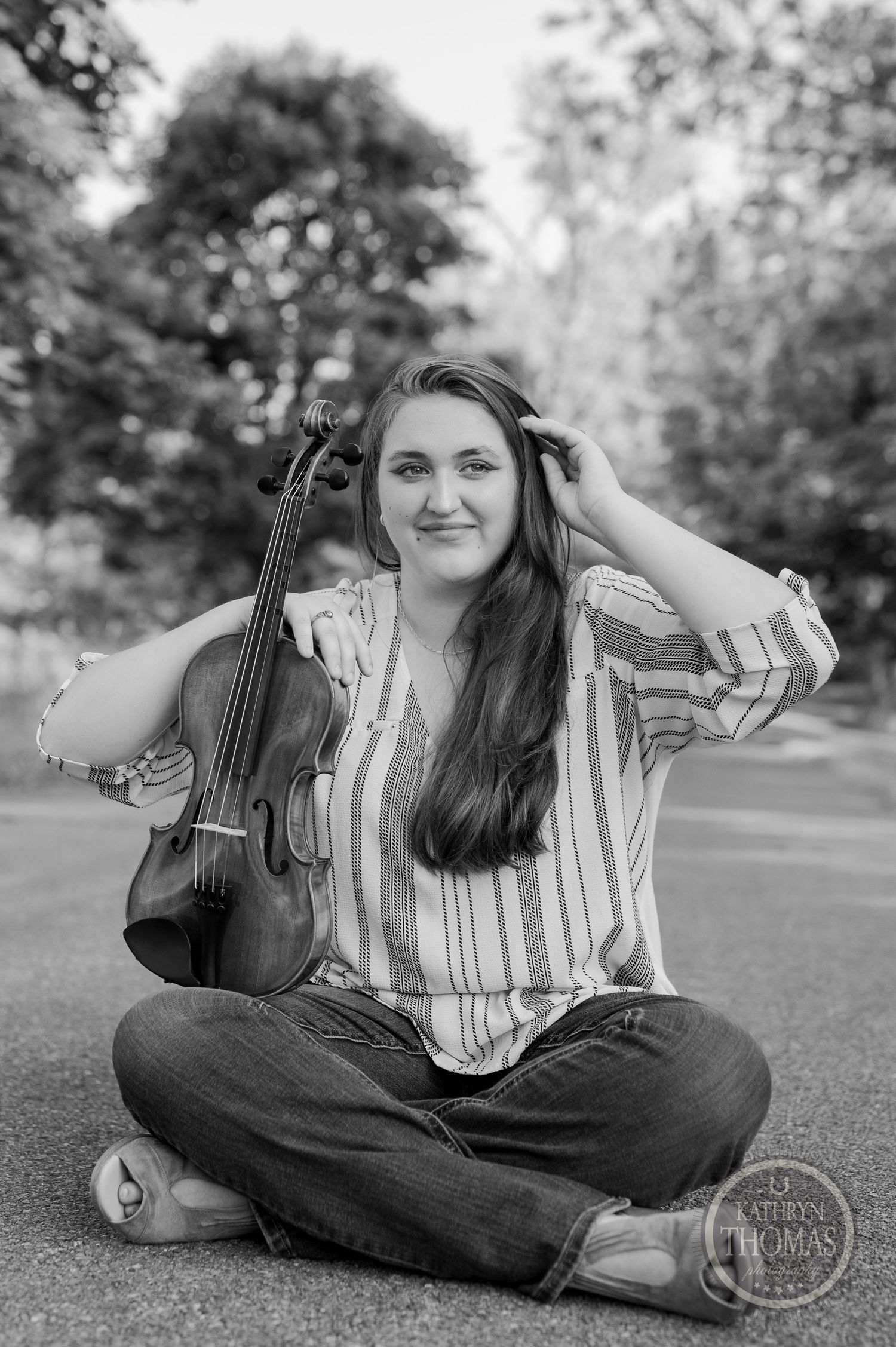 Black and white portrait of musician sitting with violin on outdoor path.